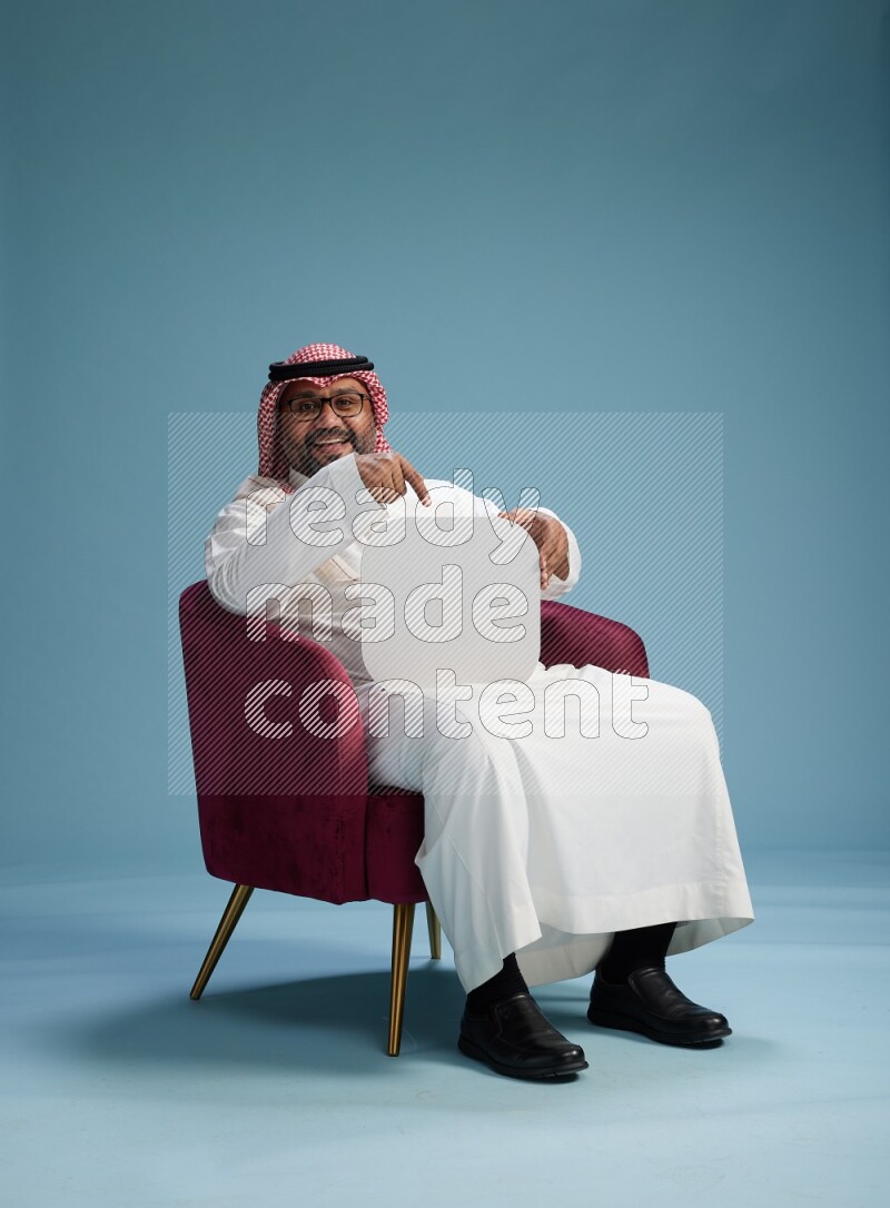 Saudi Man with shimag sitting on chair holding social media sign on blue background