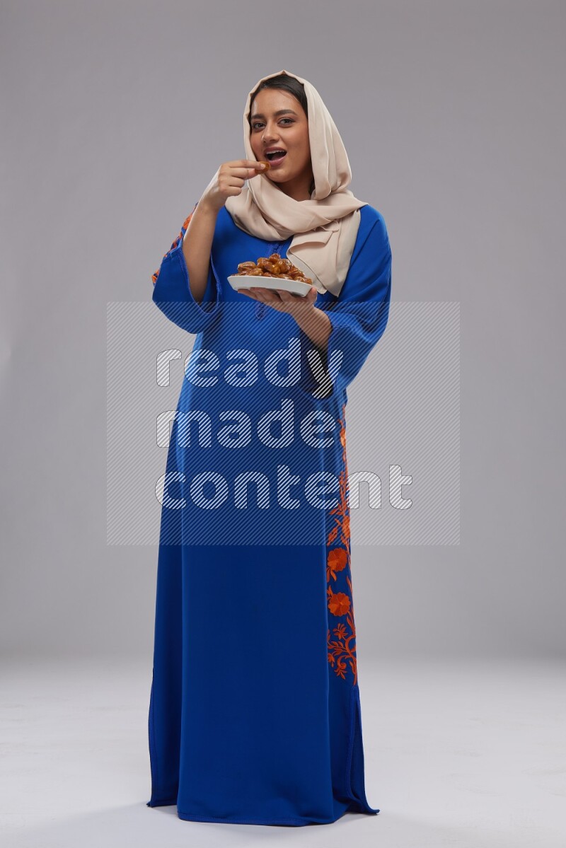 A Saudi woman standing wearing Jalabeya holding a plate of dates