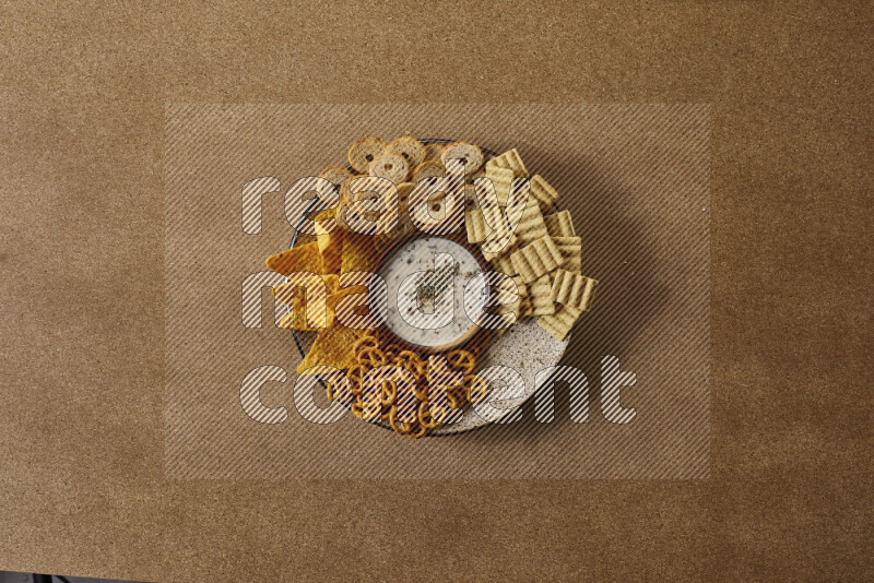 Assorted snacks on a pottery plate with a dipping on brown background