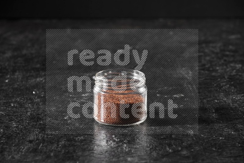 A glass jar full of garden cress seeds on a textured black flooring