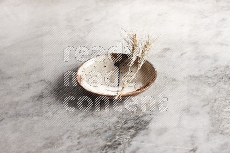 Wheat stalks on multicolored pottery plate on grey marble background