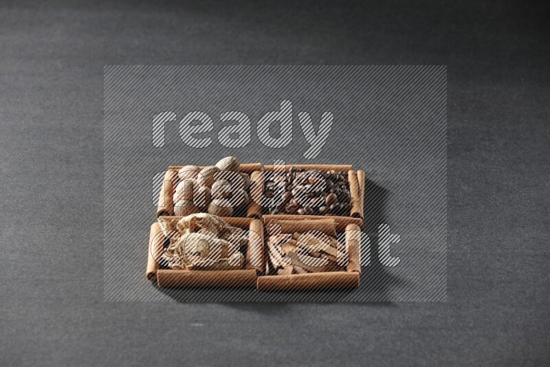 4 مربعات من عيدان القرفة ممتلئة بحبوب القهوة وقطع القرفة والزجبيل المجفف وجوزة الطيب على أرضية سوداء