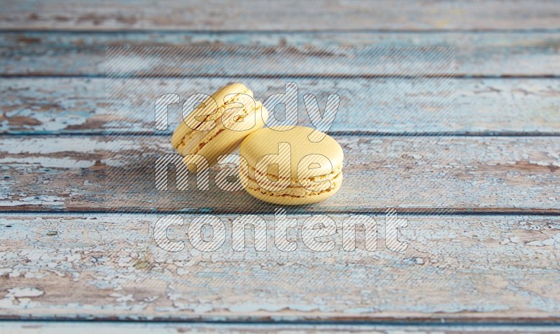 45º Shot of two Yellow Vanilla macarons on a light blue wooden background