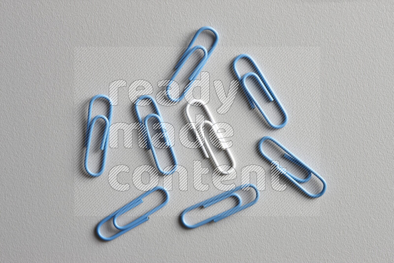 A white paperclip surrounded by bunch of blue paperclips on grey background