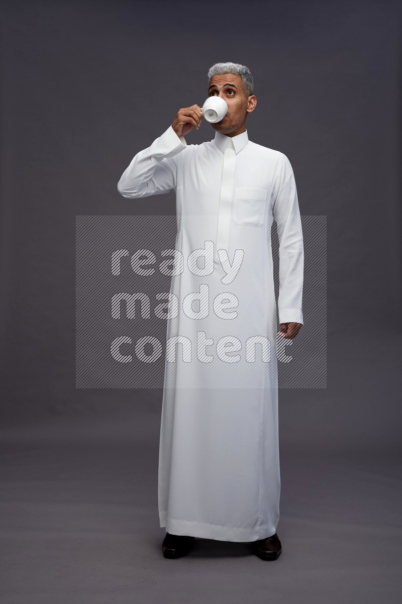 Saudi man wearing thob standing holding mug on gray background