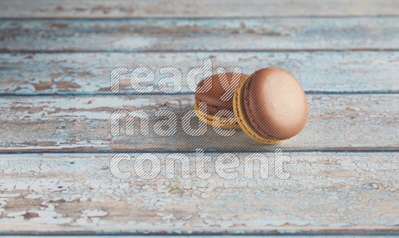45º Shot of two Yellow and Brown Chai Latte macarons on light blue wooden background