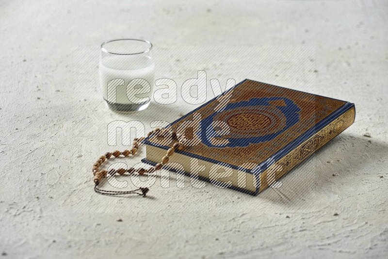 Quran with dates, prayer beads and different drinks all placed on textured white background