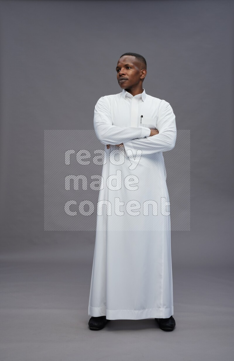 Saudi man wearing thob standing with crossed arms on gray background
