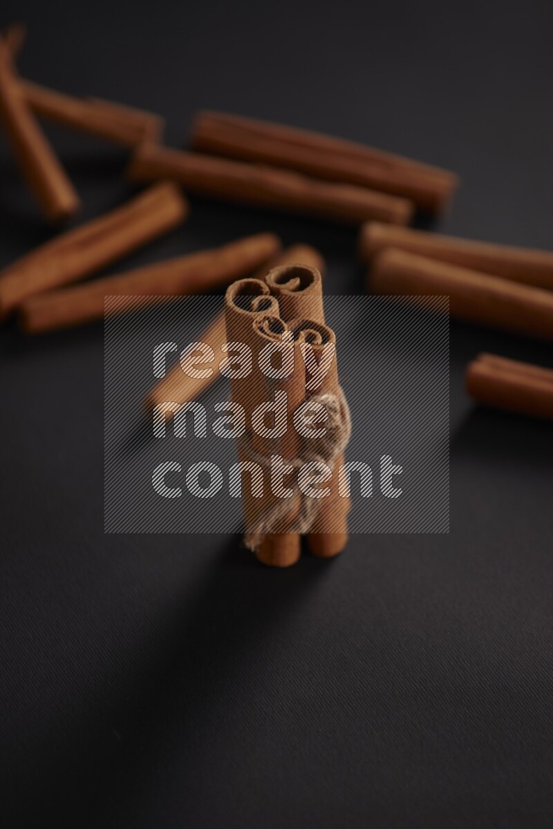 4 Cinnamon sticks stacked and bounded with more sticks in the background on black flooring