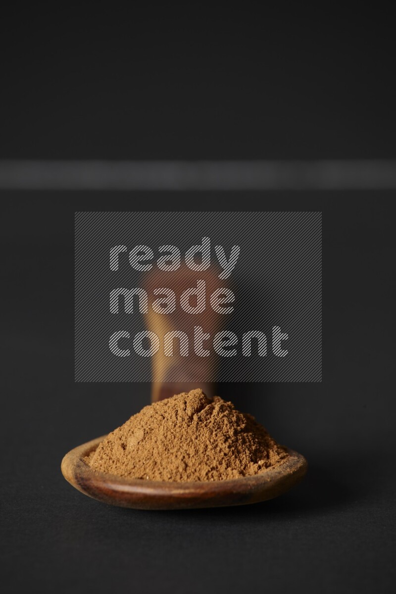 Cinnamon powder in a spoon ladle on black background
