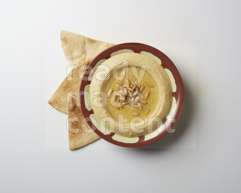 Hummus in a traditional plate garnished with pine nuts on a white background