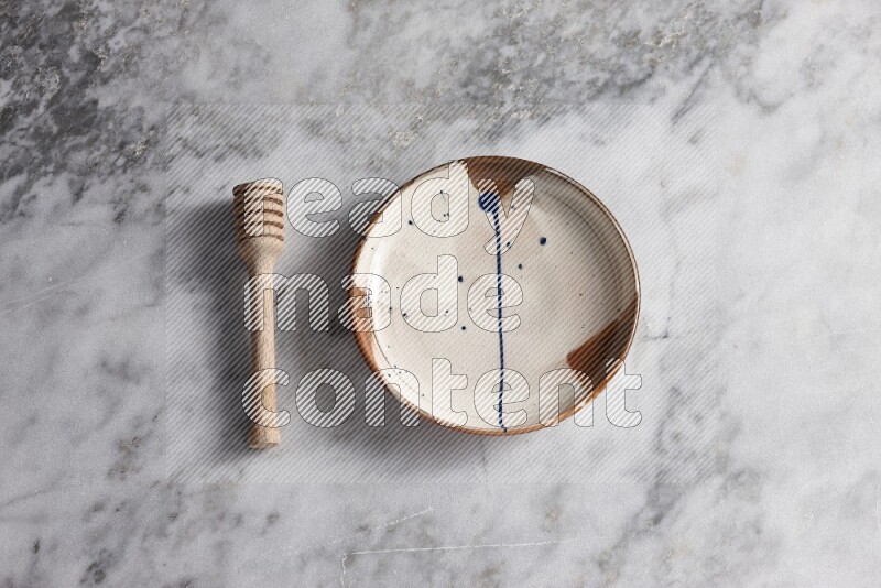 Multicolored pottery plate with wooden honey dipper on the side on grey marble background