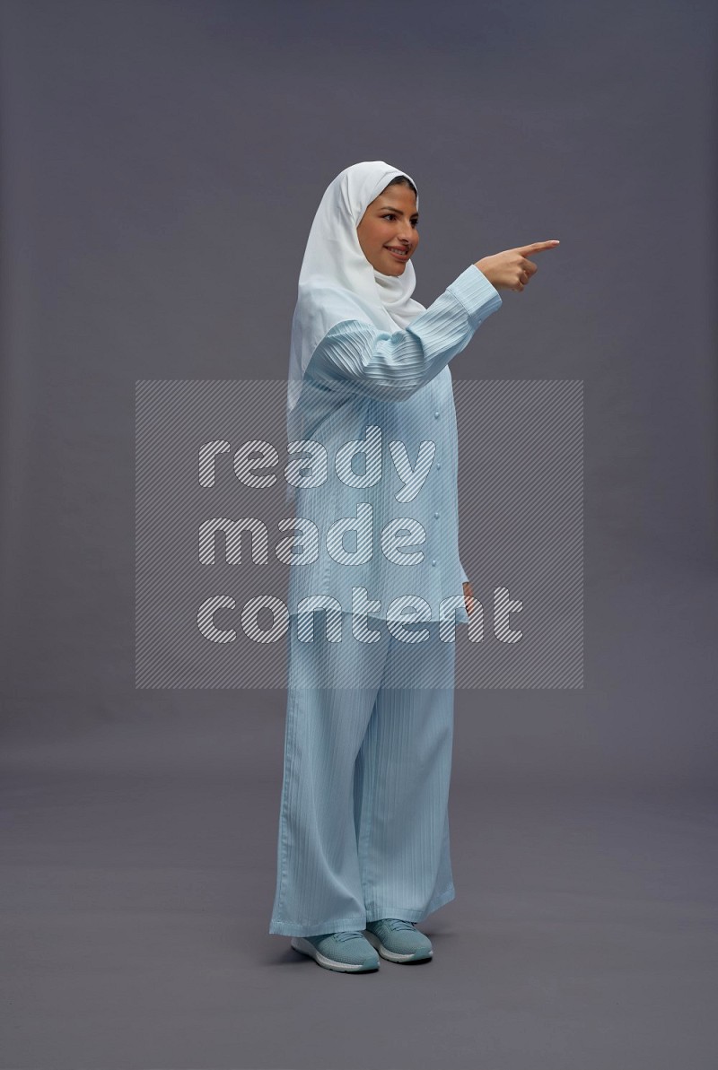 Saudi woman wearing hijab clothes standing interacting with the camera on gray background