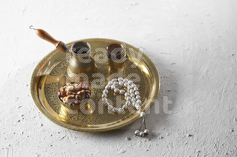 مكسرات في وعاء معدني مع قهوة وسبحة على صينية علي خلفية بيضاء