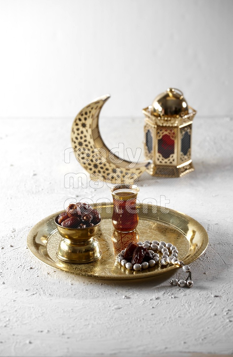 Dates in a metal bowl with tea and prayer beads on a tray beside lanterns in a light setup