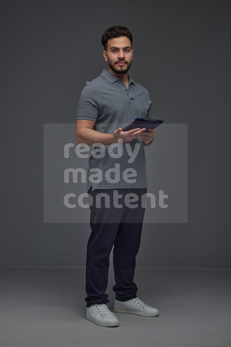 A man wearing casual standing and using his tablet and making multi hand gestures different angles eye level on a gray background