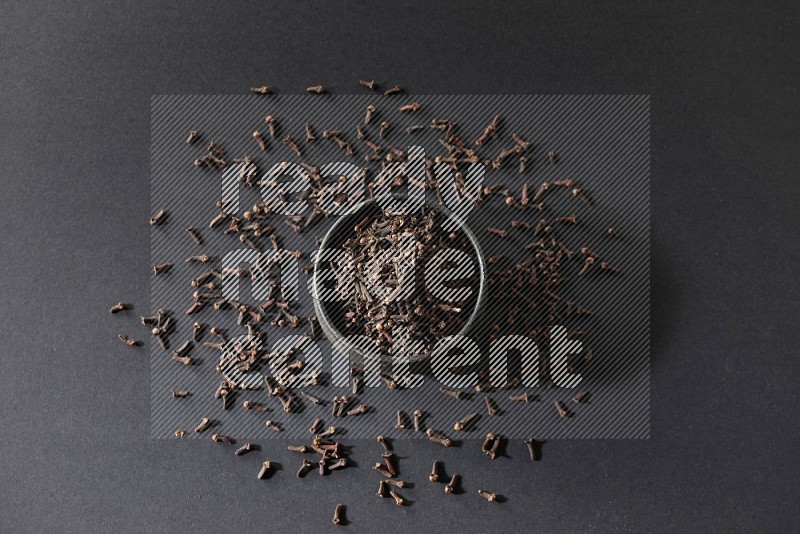 A black pottery bowl full of cloves on a black flooring