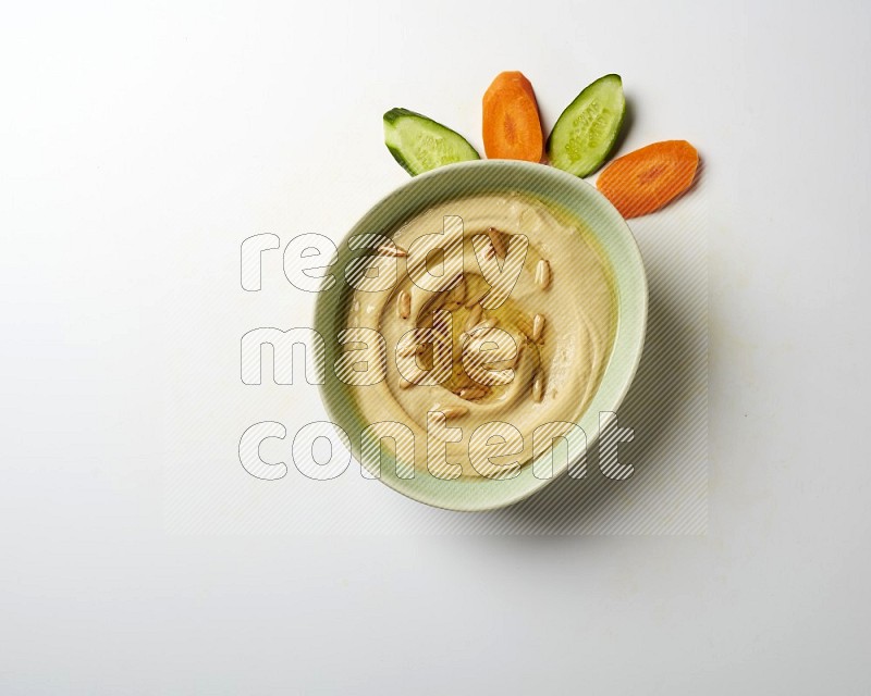 Hummus in a green plate garnished with pine nuts on a white background