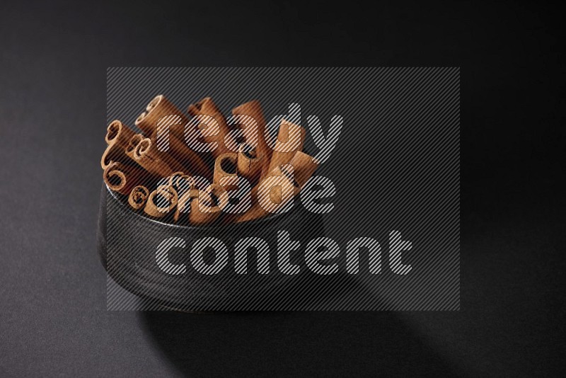 Cinnamon sticks in a black bowl on a black background in different angles