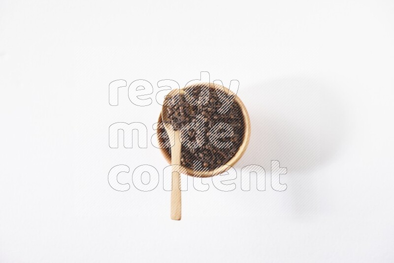A wooden bowl and a wooden spoon full of cloves on a white flooring
