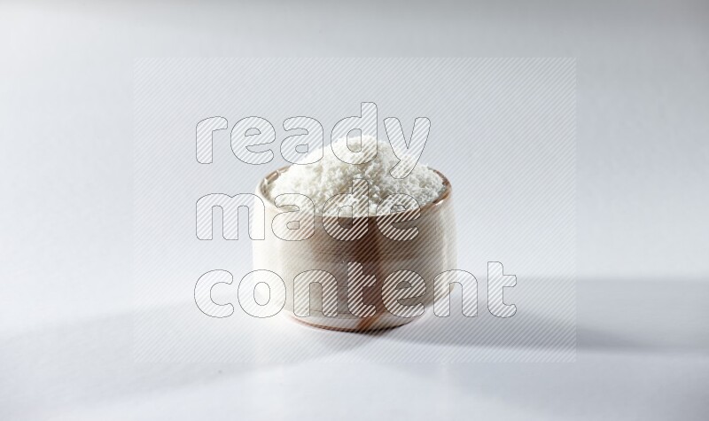 A beige ceramic bowl full of desiccated coconut on a white background in different angles