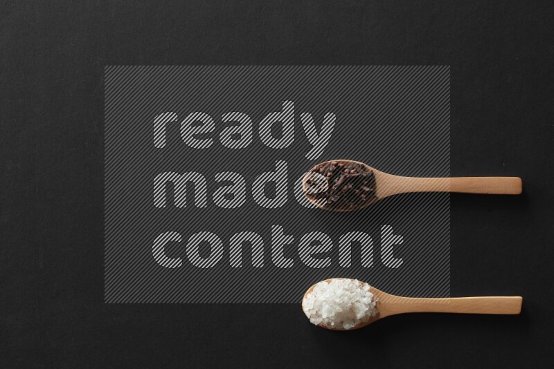 الفلفل الأبيض والقرنفل والهيل والملح والفلفل الأسود وريحان مجفف في معالق خشبية علي خلفية سوداء