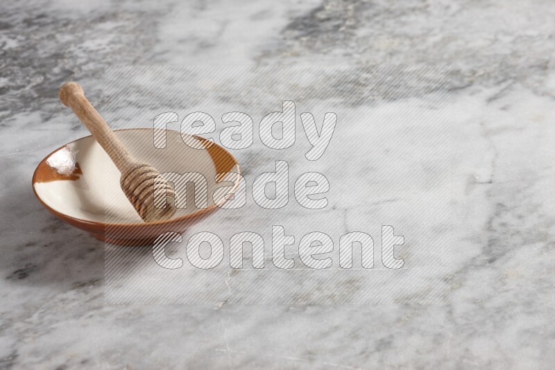 Multicolored pottery plate with wooden honey dipper in it on grey marble background