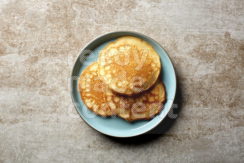 Three stacked plain pancakes in a blue plate on beige background