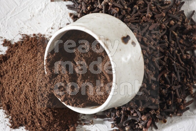 A beige ceramic bowl with cloves powder spilled out of it on a textured white flooring