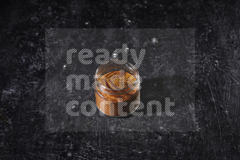 A glass jar full of ground paprika powder on black background