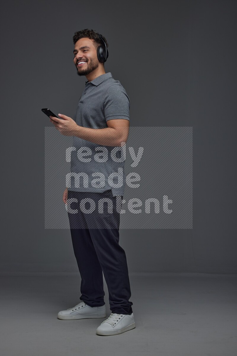 A man wearing casual and using his phone and headphone eye level on a gray background