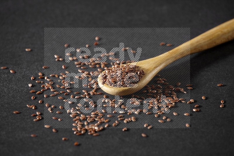 A wooden spoon full of flax and seeds spreaded beside it on a black flooring in different angles