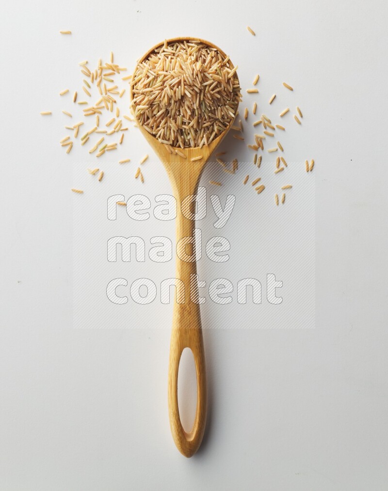 Top-view of a long grain brown rice inside a wooden spoon on white background