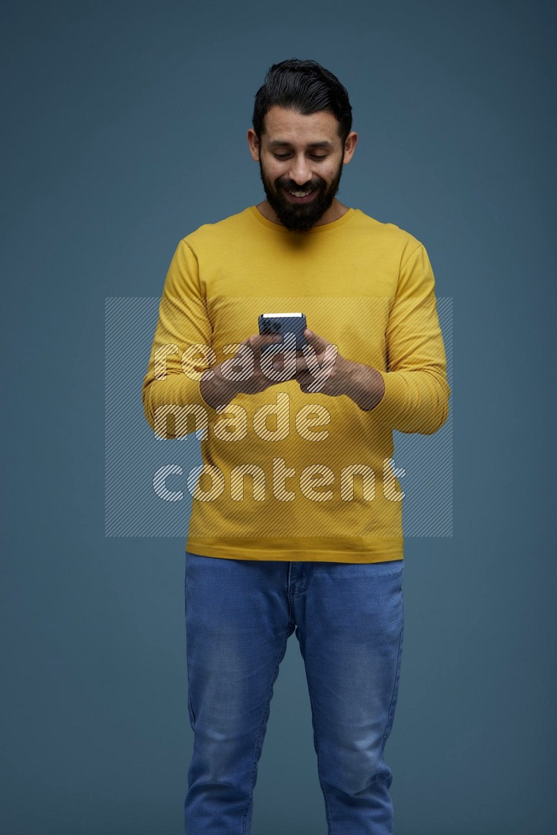 Man typing on his phone in a blue background wearing a yellow shirt