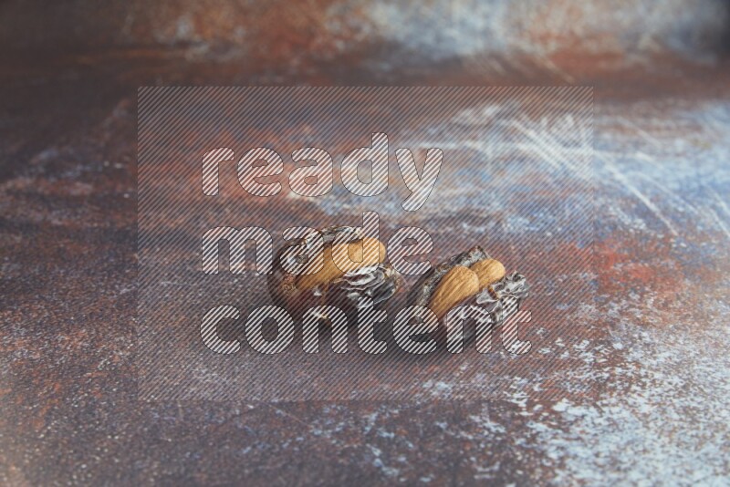 two almond stuffed madjoul dates on a rustic reddish background