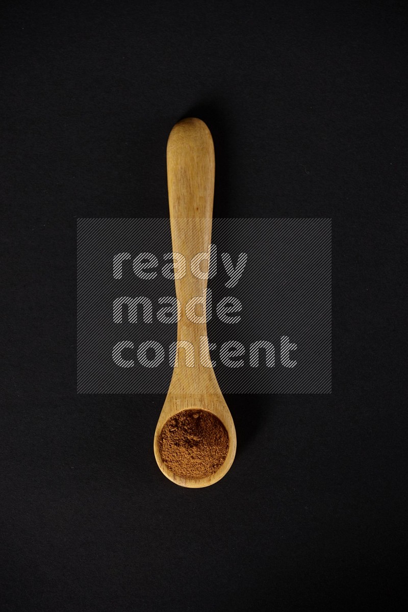 Cinnamon powder in a wooden spoon on a black background