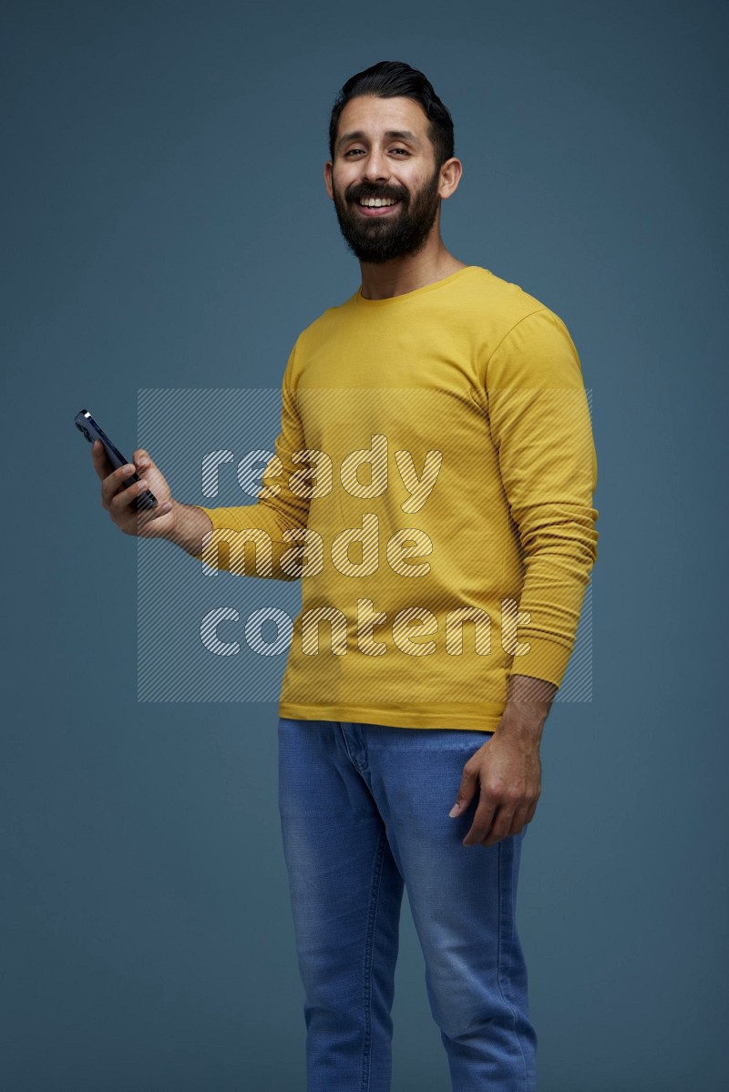 Man posing with a phone in a blue background wearing a yellow shirt