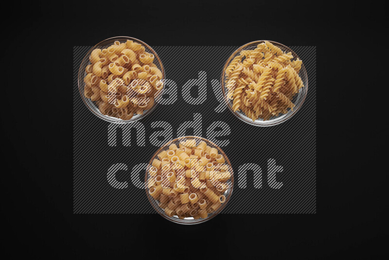 Different pasta types in glass bowls on black background