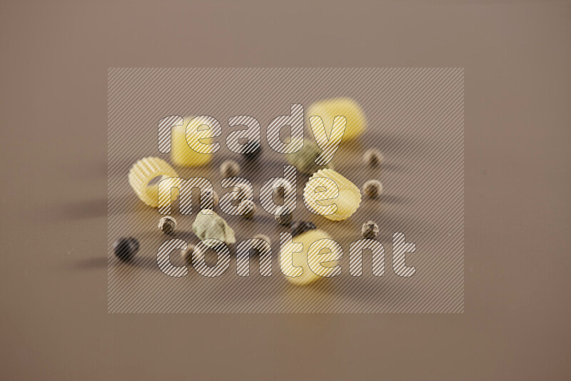 Raw pasta with different ingredients such as cherry tomatoes, garlic, onions, red chilis, black pepper, white pepper, bay laurel leaves, rosemary and cardamom on beige background