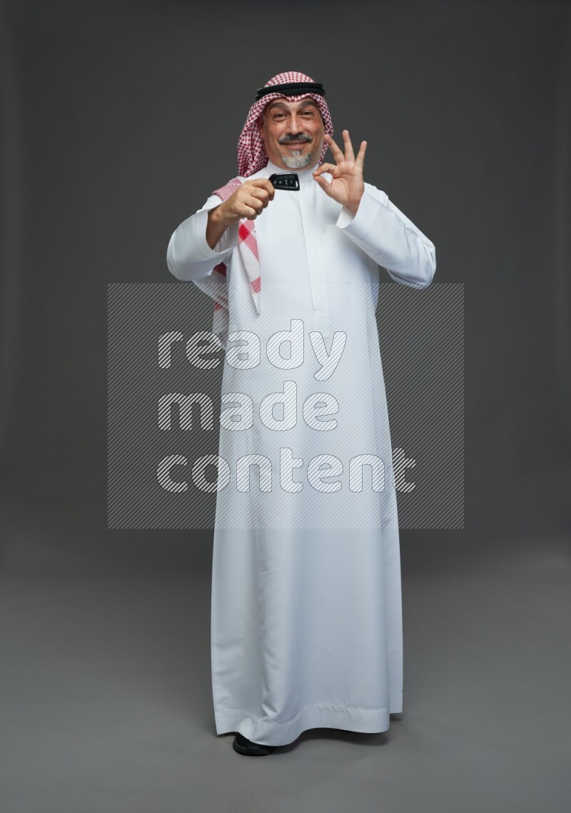 Saudi man with shomag Standing holding car key on gray background