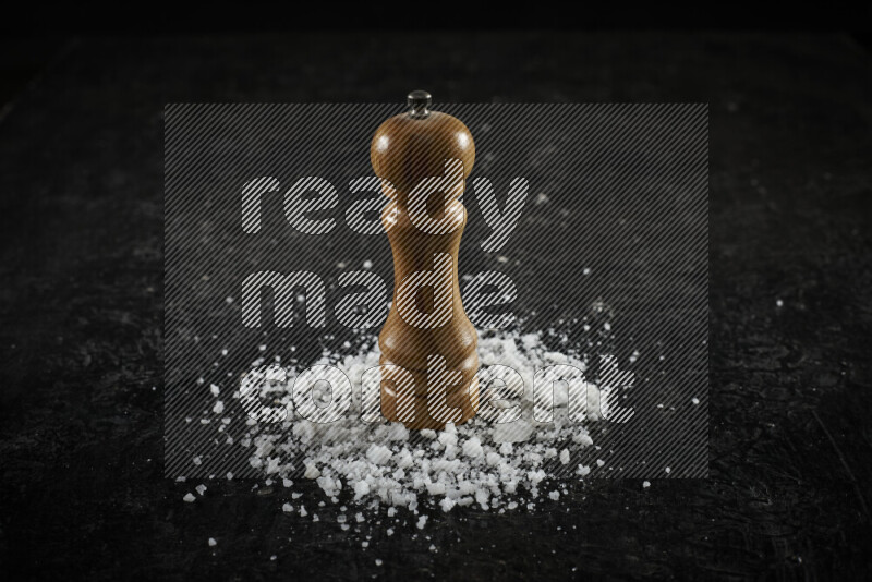 A wooden grinder standing upright and surrounded by coarse white sea salt on black background