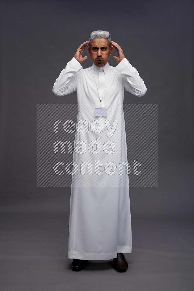 Saudi man wearing thob with neck strap employee badge standing hands on head on gray background