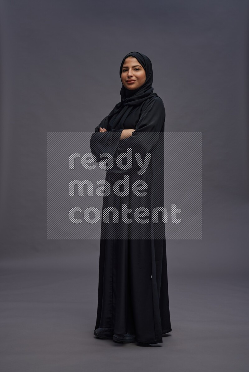Saudi woman wearing Abaya standing with crossed arms on gray background