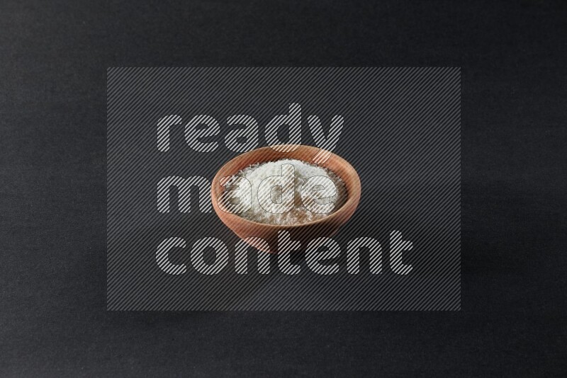 A wooden bowl full of desiccated coconut on a black background in different angles