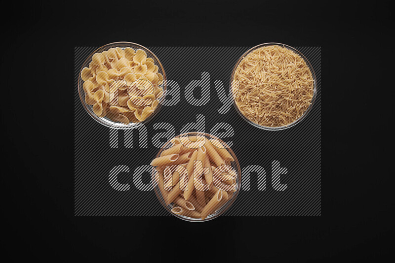 Different pasta types in glass bowls on black background