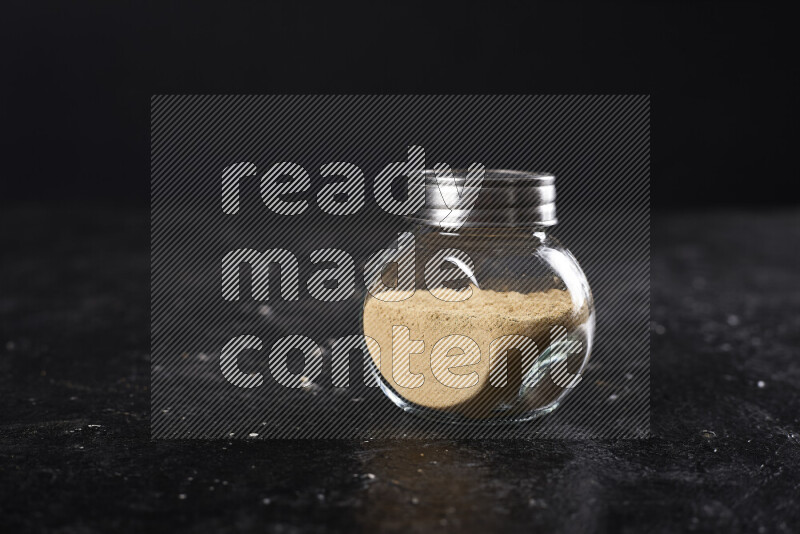 A glass jar full of ground ginger powder on black background