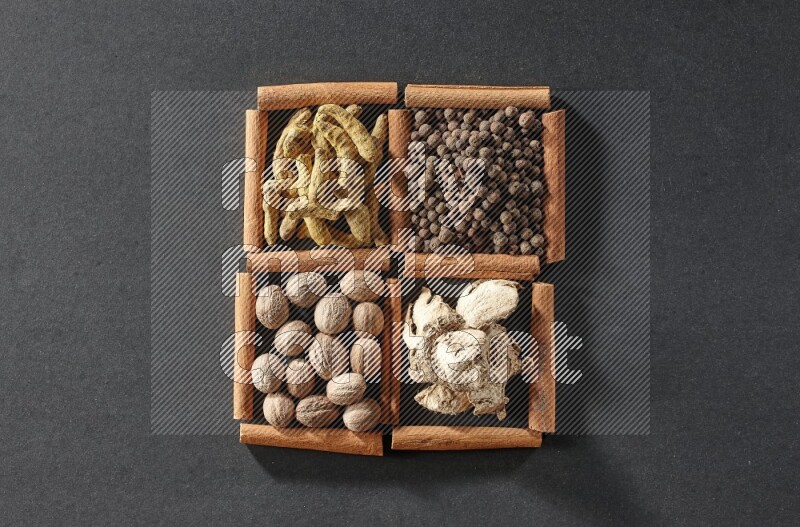 4 squares of cinnamon sticks full of turmeric fingers, allspice, dried ginger and nutmegs on black flooring