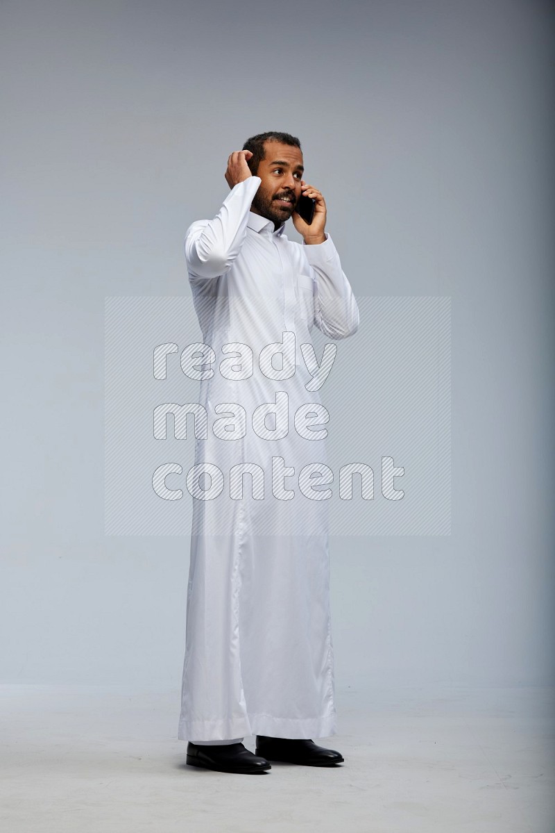 Saudi man wearing Thob standing talking on phone on Gray background