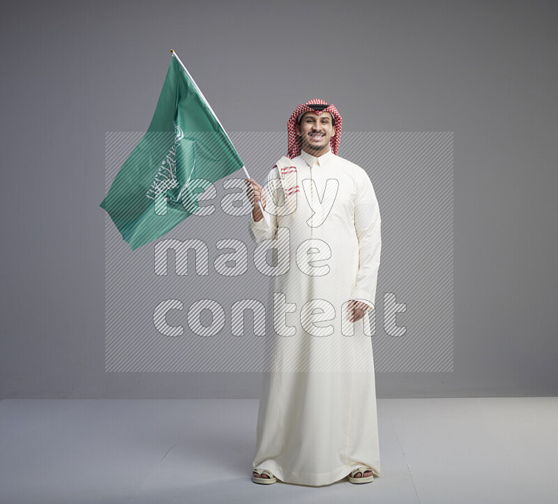 رجل سعودي يرتدي ثوب ابيض وشماغ احمر يحمل علم السعودية