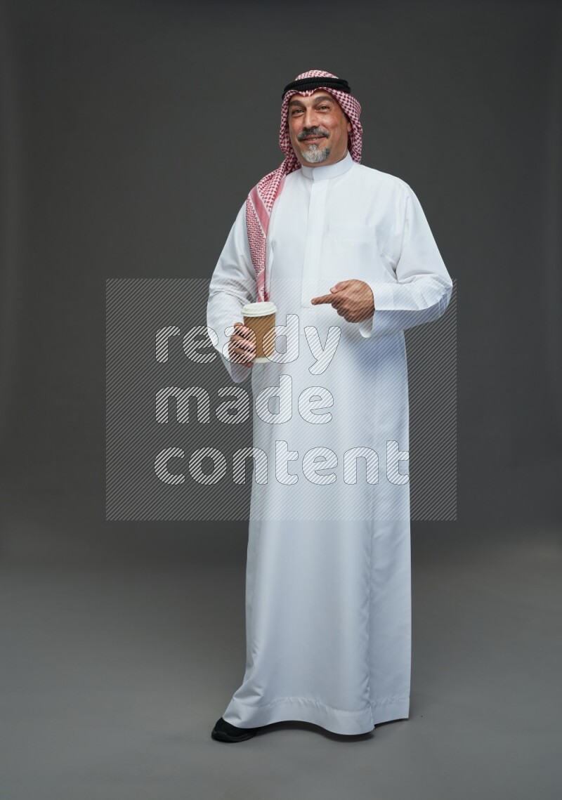 Saudi man with shomag Standing holding paper cup on gray background
